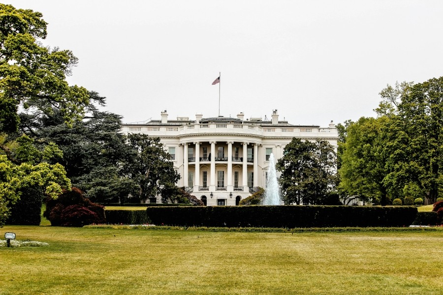 Photo of the White House, a multi-storey building with columns and an American flag on its roof. 